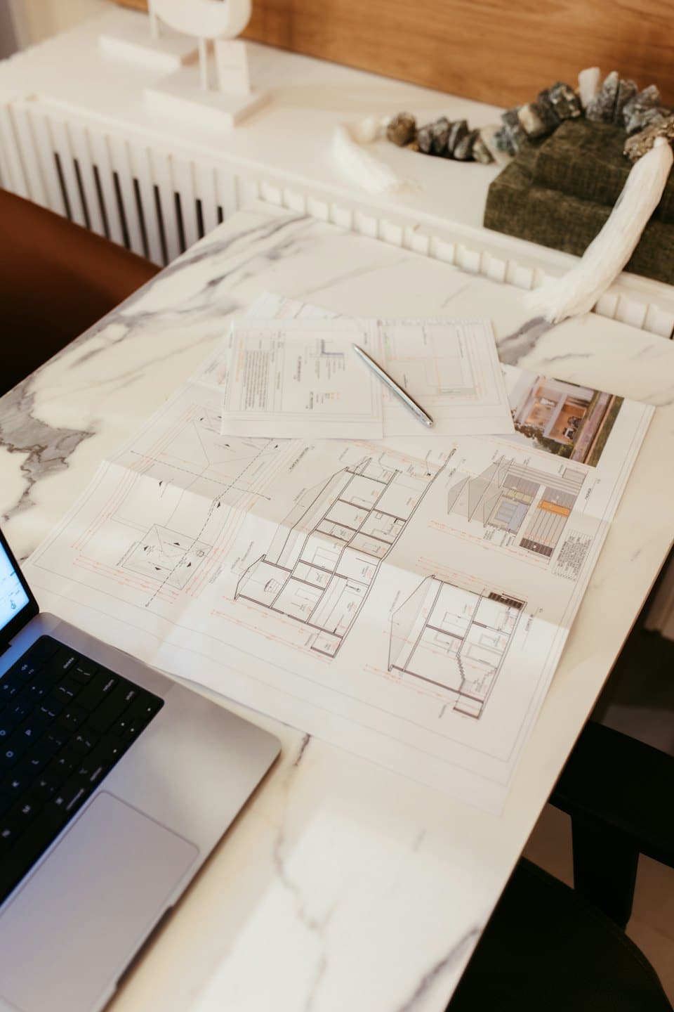 Architektonické plány a notebook na mramorovom stole.